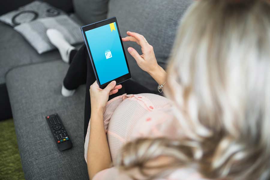 Uma mulher grávida deitada num sofá e usando o Journey num tablet.